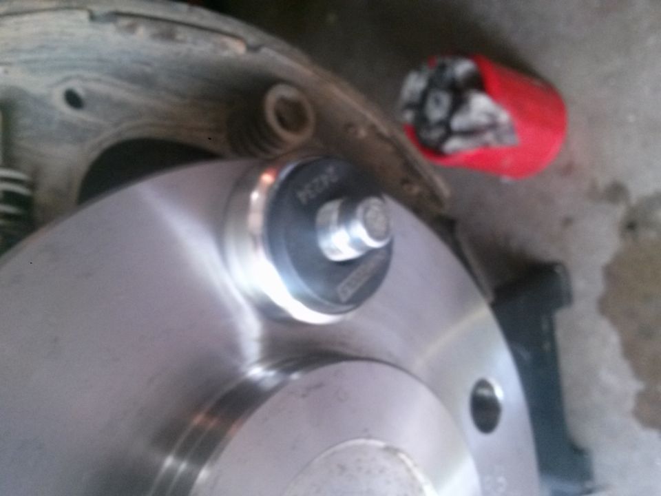 close-up of vehicle brake rotor with part number visible, red cap in background