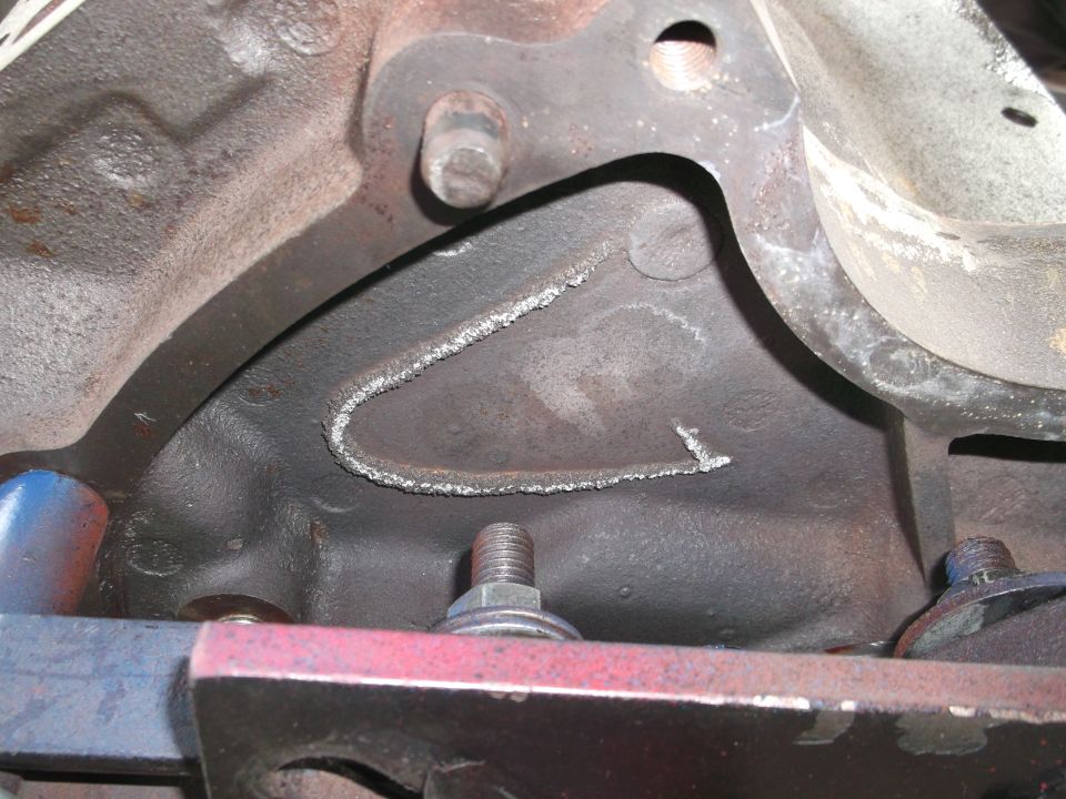 Close-up of cast iron engine block with a curved weld repair bead across a crack, bolts and red bracket nearby