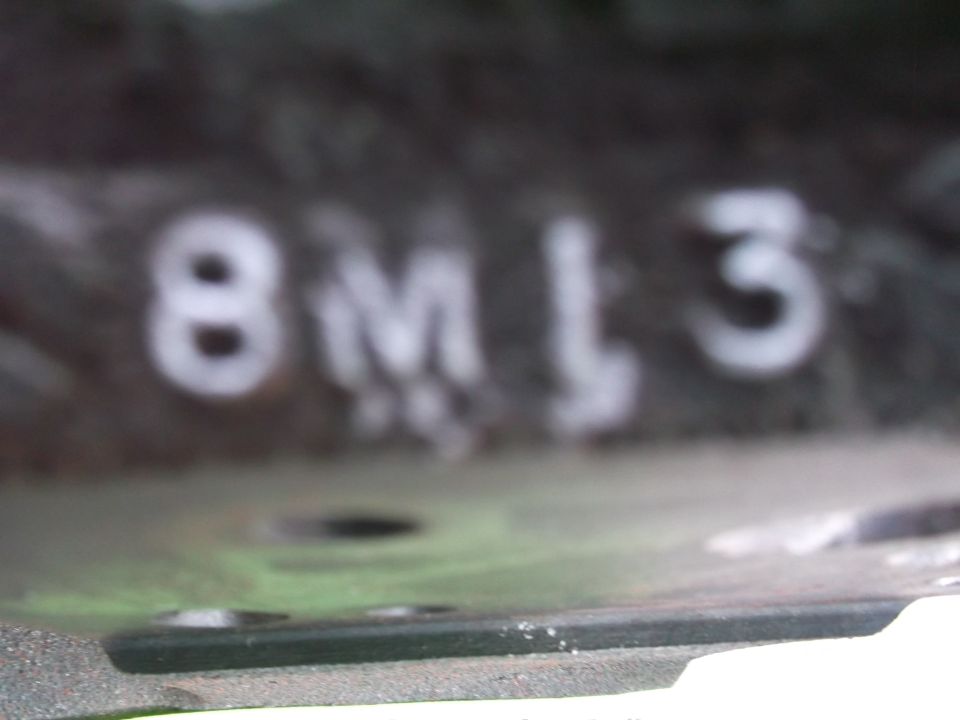 Blurry close-up of white "8M13" casting code stamped on dark engine part