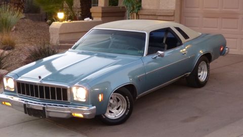 1975 Chevrolet Chevelle - A light blue 1975 Chevrolet Chevelle coupe with a tan vinyl roof is parked in front of a garage and house.