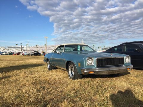 1975 Chevrolet Chevelle - A light blue 1975 Chevrolet Chevelle coupe with a white vinyl top is seen from a three-quarter front view on a grassy field.