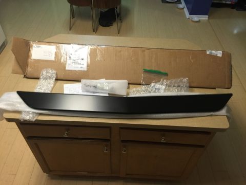 1975 Chevrolet Chevelle - A black car trim piece is shown in its packaging, resting on a table.