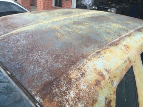 1975 Chevrolet Chevelle - The heavily rusted roof of a car shows significant deterioration with patches of yellowing paint.