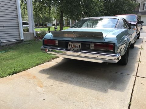 1975 Chevrolet Chevelle - The rear of a light blue coupe is visible, parked next to a house and a red truck.