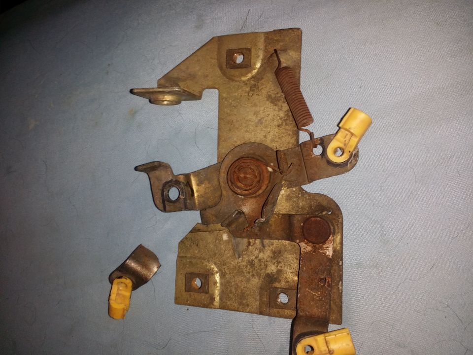 Close-up of a rusty metal hood latch mechanism with yellow plastic components and a spring