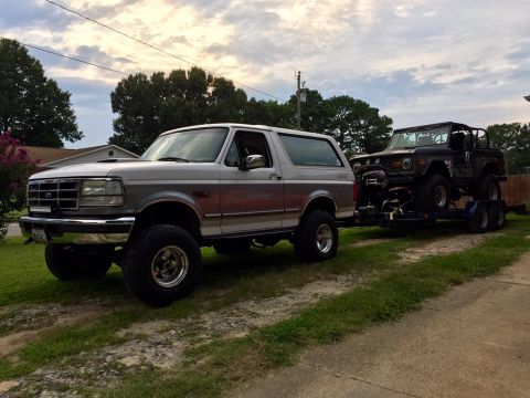 1972 Ford Bronco - A silver Ford Bronco from the mid-1990s tows a heavily modified Jeep on a trailer.