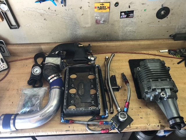 Supercharger, intake manifold, and other engine parts laid out on a workbench