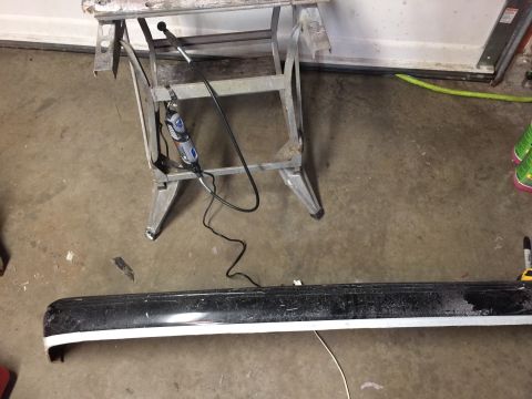 1983 Ford Mustang - Car bumper and Dremel tool on a sawhorse, likely in a garage or workshop setting.