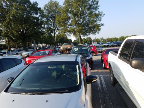 1988 Ford Bronco - A variety of vehicles are parked in an outdoor lot under trees on a sunny day.