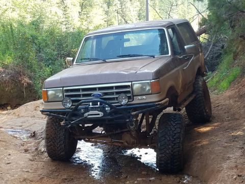 1988 Ford Bronco - This lifted SUV navigates a muddy trail, its off-road capabilities and design.