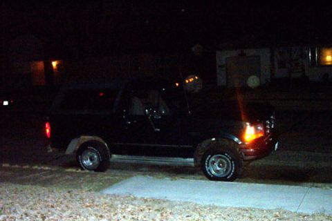 1995 Ford Bronco - A black Ford Bronco is parked in a driveway at night with its headlights on.