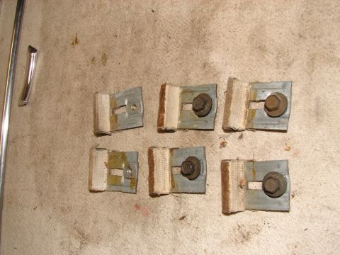 1973 Ford Ranchero - Six metal brackets with fabric and bolts are laid out on a textured surface. A chrome trim piece and a metal rod are visible on the left si…