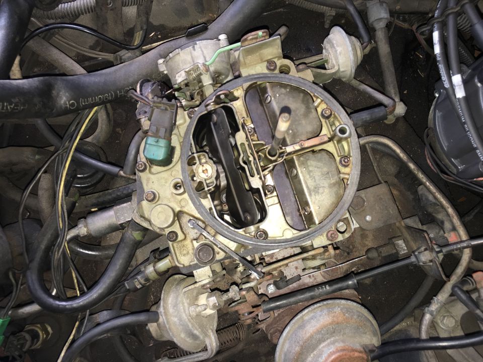 Close-up of a vehicle carburetor with hoses, wires, and distributor cap.