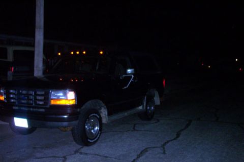 1995 Ford Bronco - Black 1995 Ford Bronco parked on cracked pavement at night.