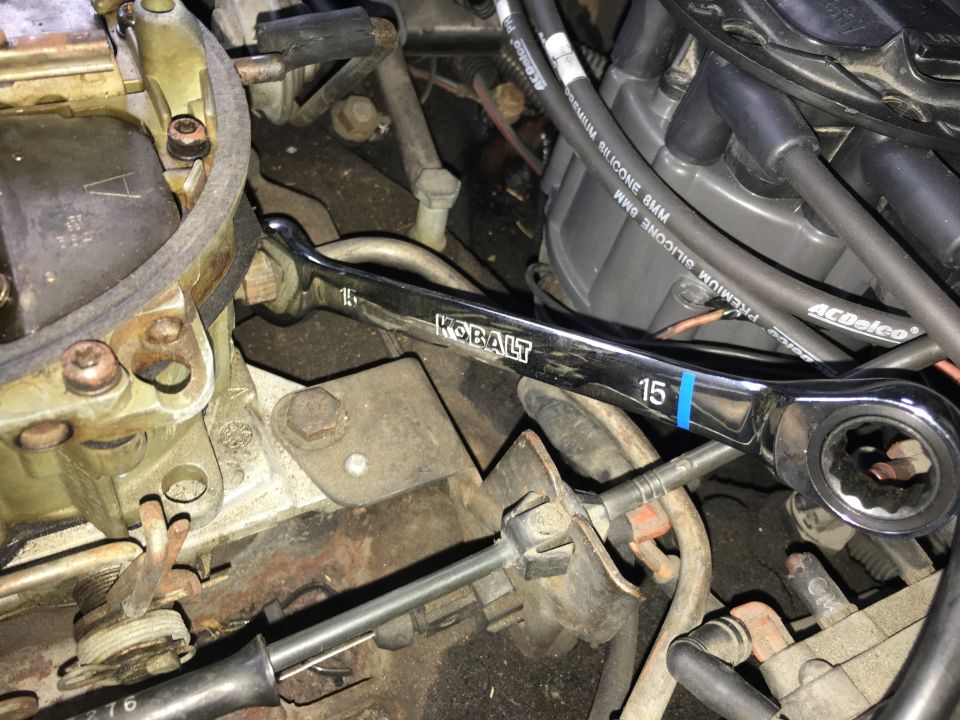 15mm Kobalt ratcheting wrench on a carburetor bolt in a cluttered engine bay.