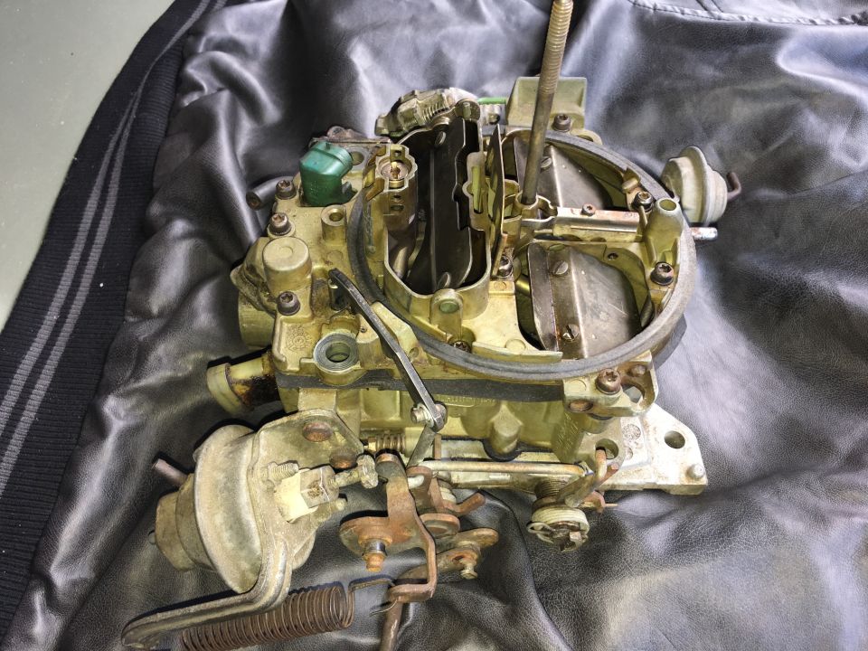 Disassembled brass and aluminum carburetor on a black textured surface.