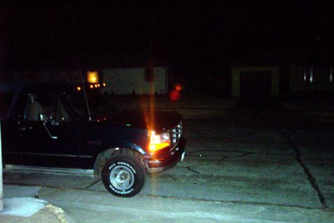 1995 Ford Bronco - A dark blue Ford F-Series truck is parked outside at night, with its headlights on.