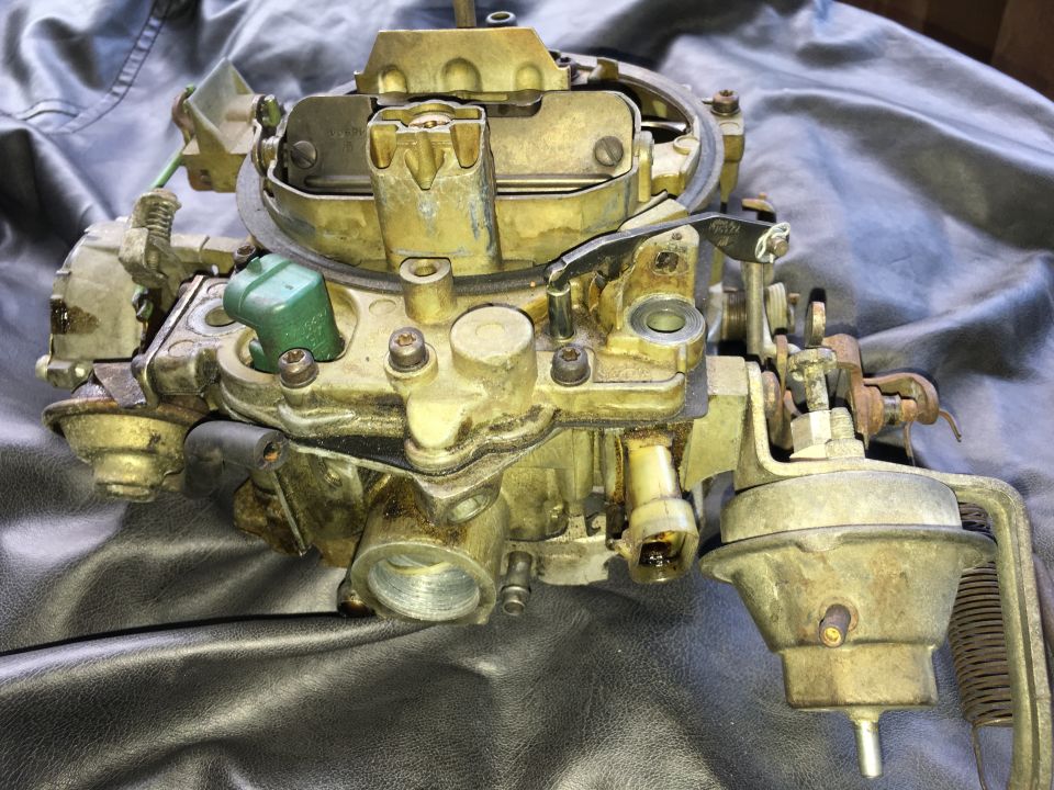 Brass-colored carburetor with green electrical component on black surface