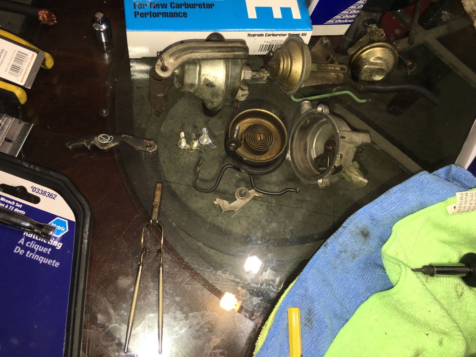 Carburetor parts and tools on a glass table.