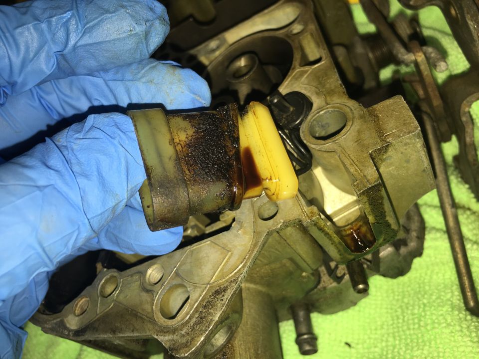 Close-up of a dirty carburetor float being held by a gloved hand.