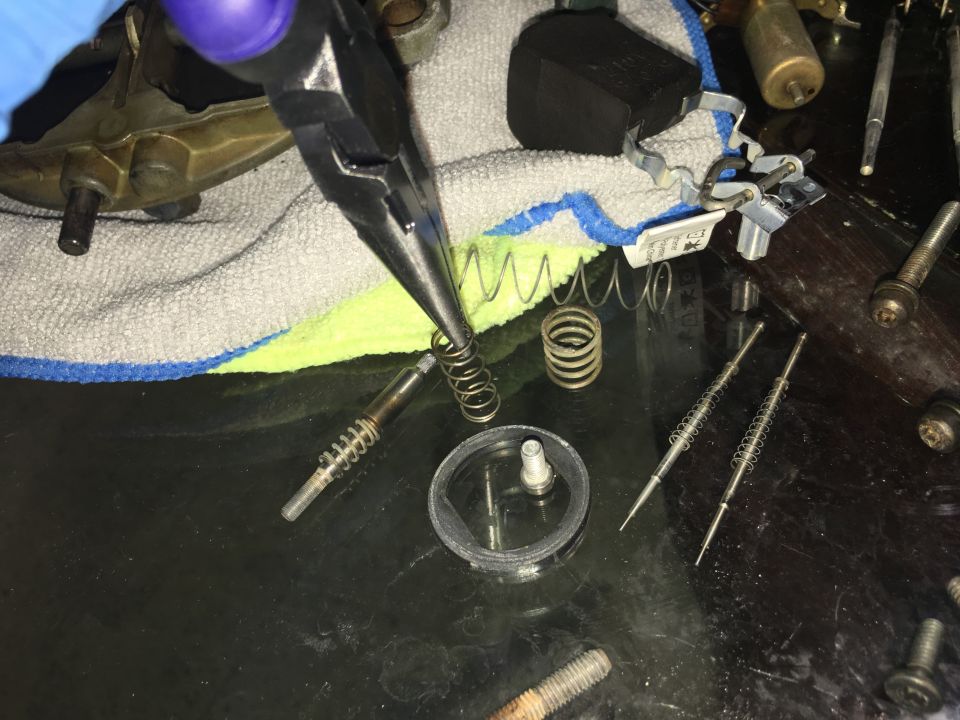 Close-up of carburetor parts and springs being worked on with pliers.