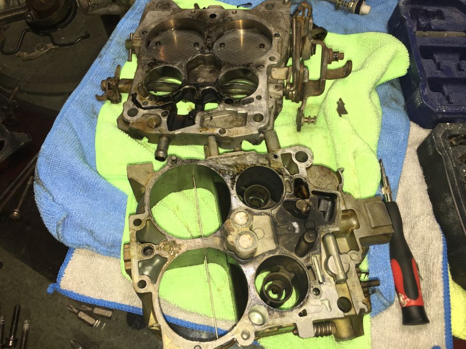 Disassembled four-barrel carburetor body and throttle plate on green and blue towels