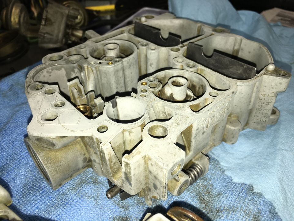 Carburetor part with visible casting numbers and springs, resting on a blue cloth