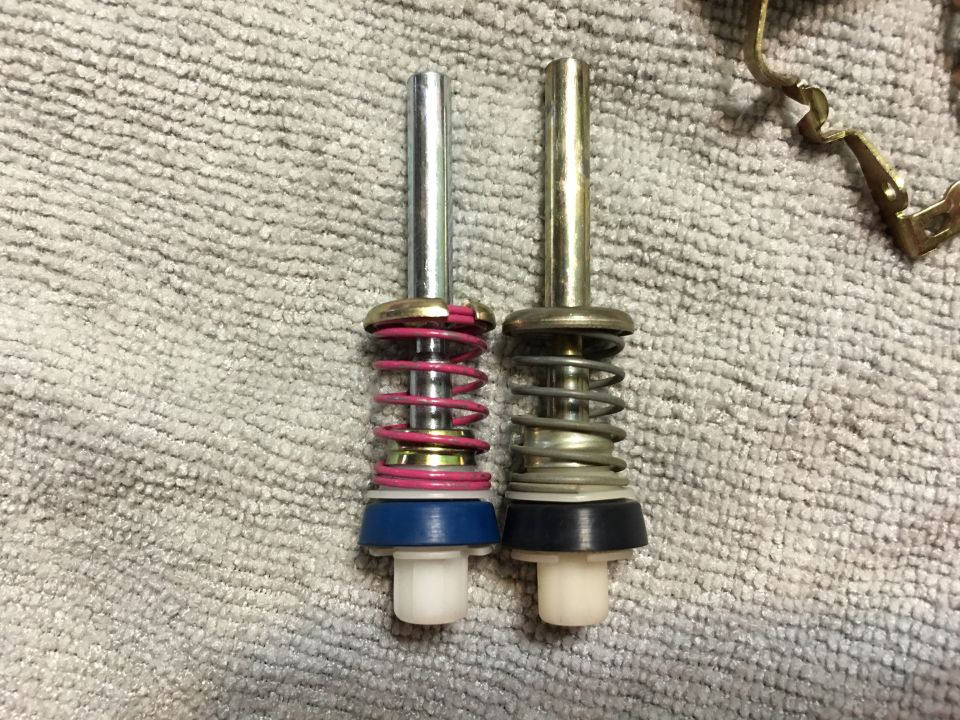 Two metal plungers with springs and rubber seals on a textured surface.