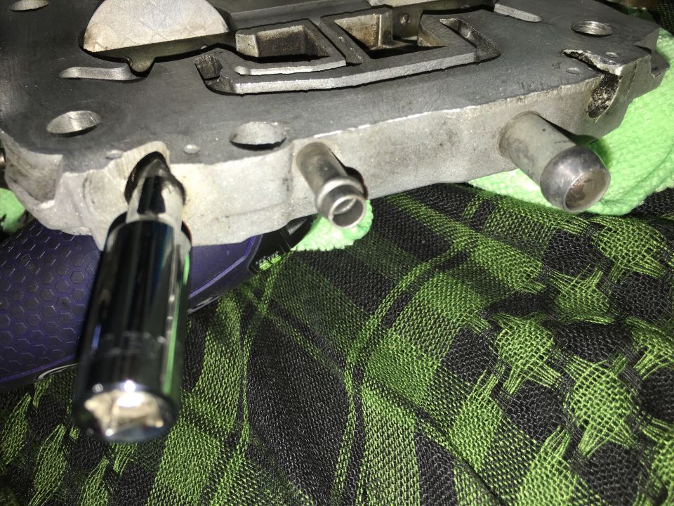 Close-up of a metal carburetor or intake manifold with a socket wrench inserted.