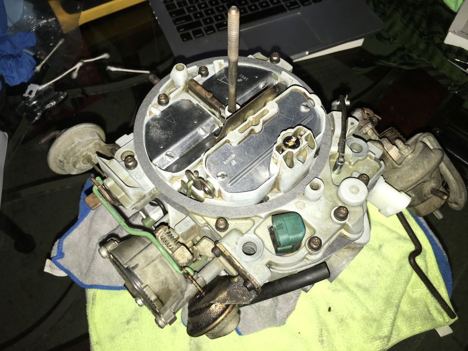 Close-up of a disassembled carburetor on a cloth, with a laptop in the background.