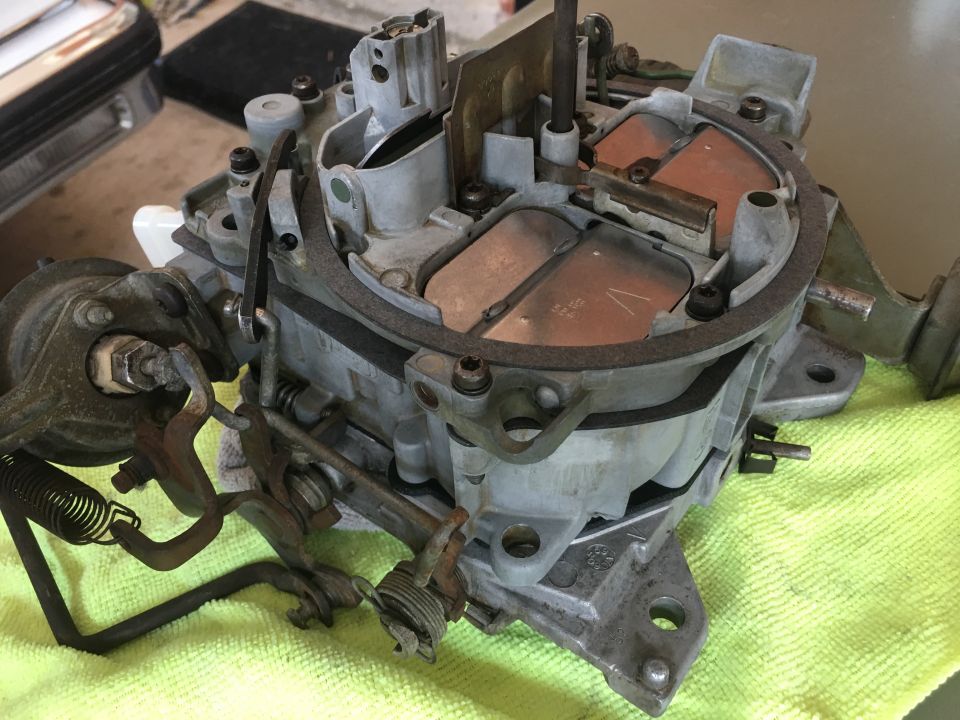 Disassembled gray metal carburetor with copper accents on a green cloth.