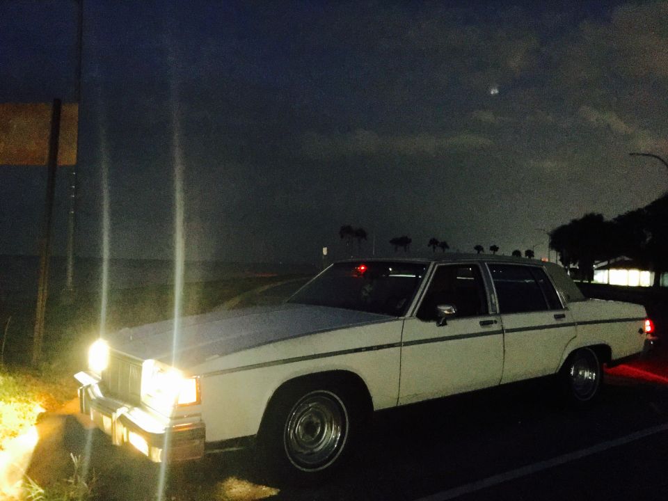 White four-door sedan parked at night with headlights on.