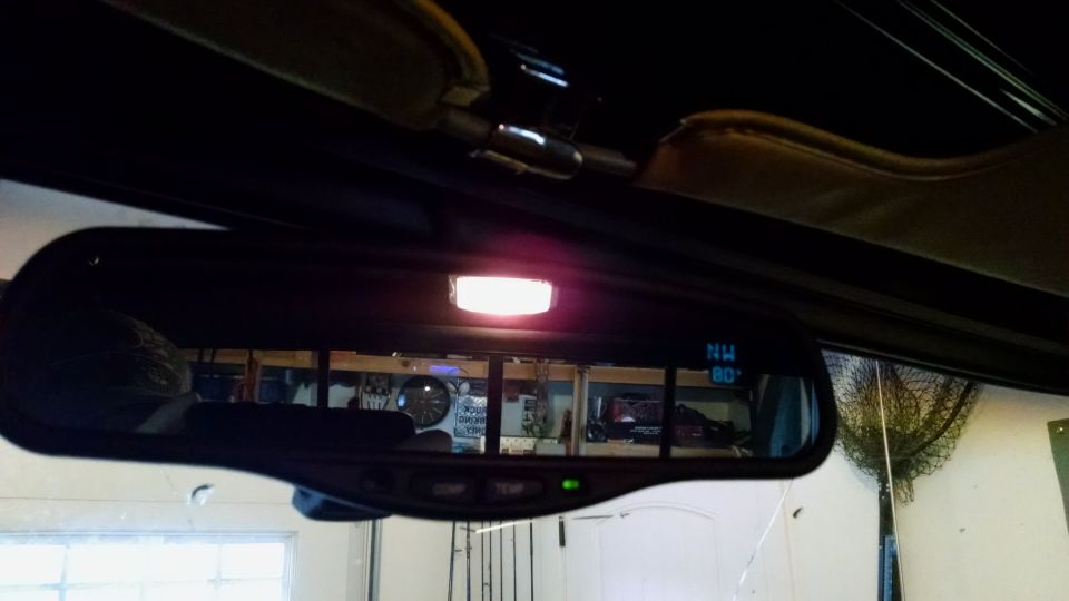 Interior rearview mirror with compass and temperature display, illuminated by a pink light.