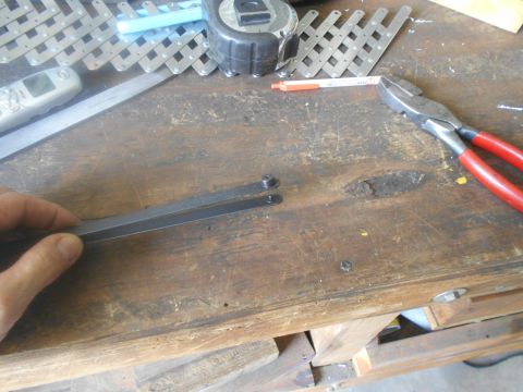 1992 Ford Bronco - A person's hand is holding two flat metal pieces with holes in them over a wooden workbench. Various tools, including pliers and a tape mea…