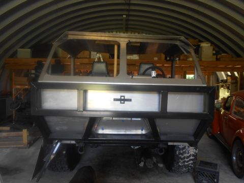 1992 Ford Bronco - The rear of a custom-built, unfinished vehicle with a metal frame and aluminum panels sits inside a Quonset hut. A red Volkswagen Beetle is…