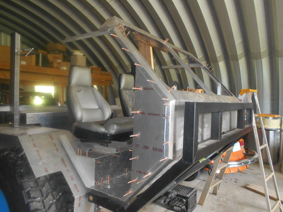 Custom vehicle frame with roll cage, bucket seats, and aluminum panels under construction.