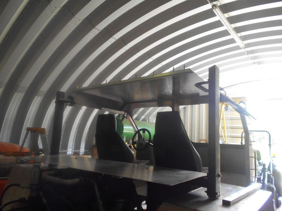 Interior of a custom vehicle with black seats and metal roof in a Quonset hut.