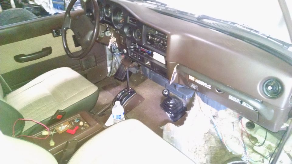 Brown interior of a Toyota Land Cruiser with dash partially disassembled, exposed wiring, and floor shifters.