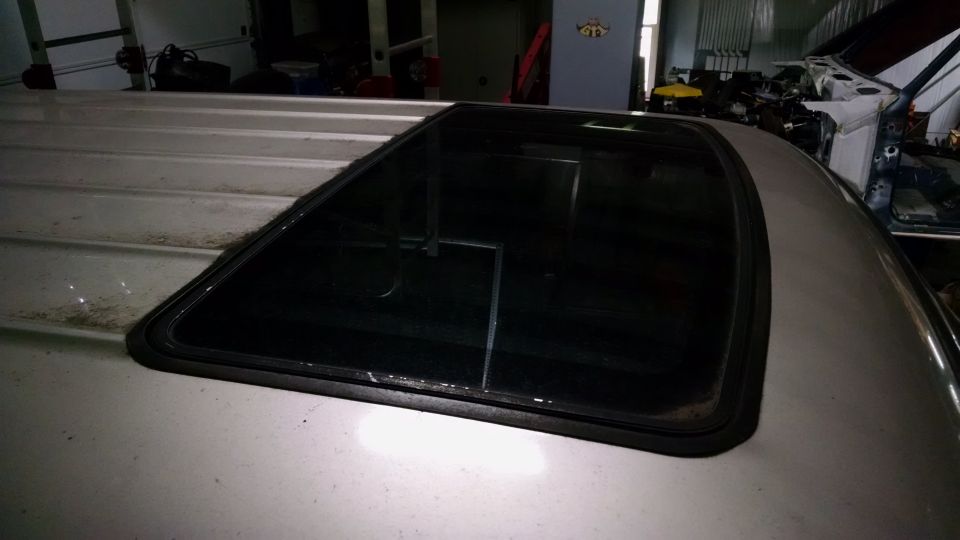 Tinted sunroof with black trim in the tan roof of a vehicle, photographed in a garage