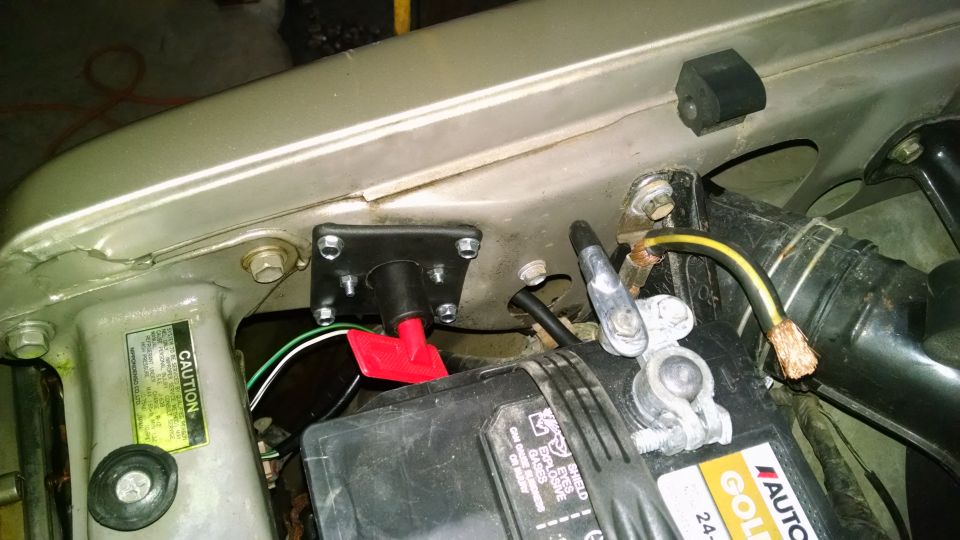 Engine bay with Autocraft Gold battery, red disconnect switch on black bracket, and exposed copper cable end.