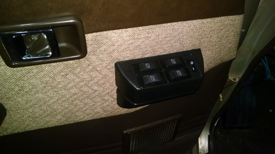 Black 4-button power window switch pod mounted on tan carpeted door panel with brown door handle