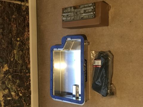 1995 Ford Bronco - A new aluminum transmission pan with a blue gasket is laid out on a carpeted floor next to a boxed transmission valve body and a plastic-wr…