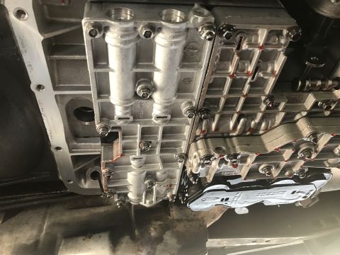 1995 Ford Bronco - Underside view of a vehicle's automatic transmission valve body and pan. The valve body is silver and shows multiple ports and bolts, with…