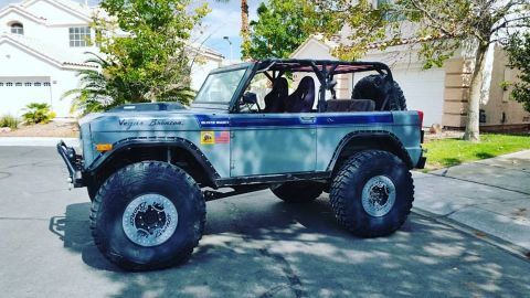 1979 Ford Bronco - A modified light blue 1979 Ford Bronco with large off-road tires and a roll cage is parked in a suburban driveway. The side of the vehicle…