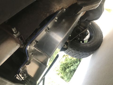 1995 Ford Bronco - Underside view of a vehicle showing an aftermarket aluminum skid plate bolted to the frame, with a tire and suspension components visible i…