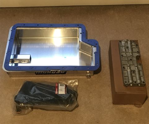 1995 Ford Bronco - A silver oil pan with a blue gasket and a metal component on a brown box are laid out on a carpeted surface.