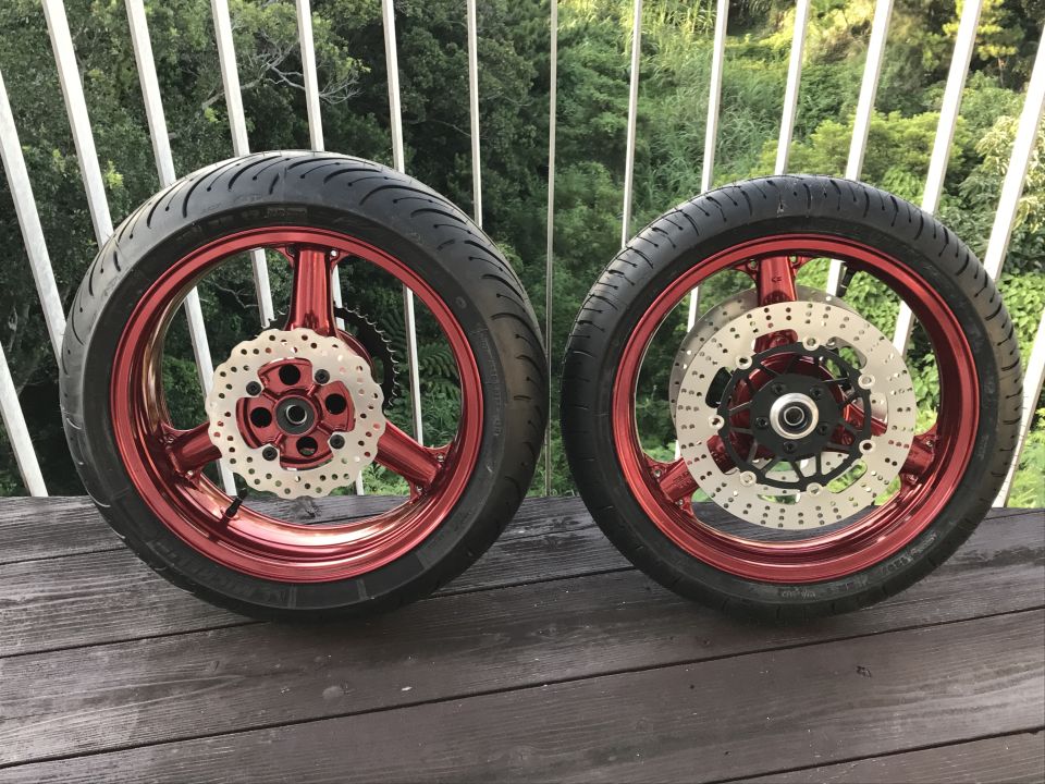 Two red motorcycle wheels with tires and brake discs on a wooden deck.