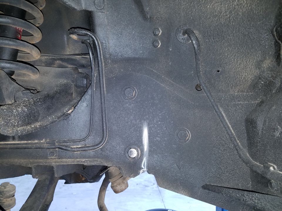 Underside of a vehicle frame with suspension and brake lines visible.