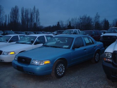 1999 Ford Crown Victoria - A blue Ford Crown Victoria is parked in a lot with other vehicles under a cloudy sky.