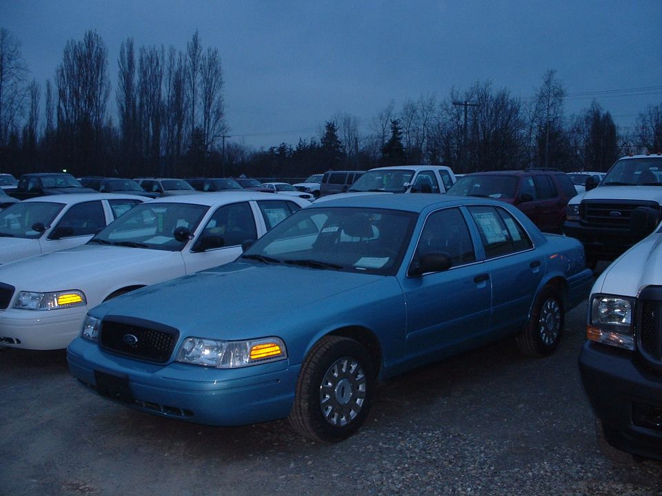 Blue Ford Crown Victoria parked in a lot with other vehicles under a cloudy sky